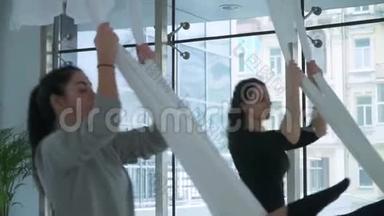 两个女人在<strong>吊床</strong>上徘徊，在<strong>室内</strong>工作室放松瑜伽。 运动女孩练习空中瑜伽。